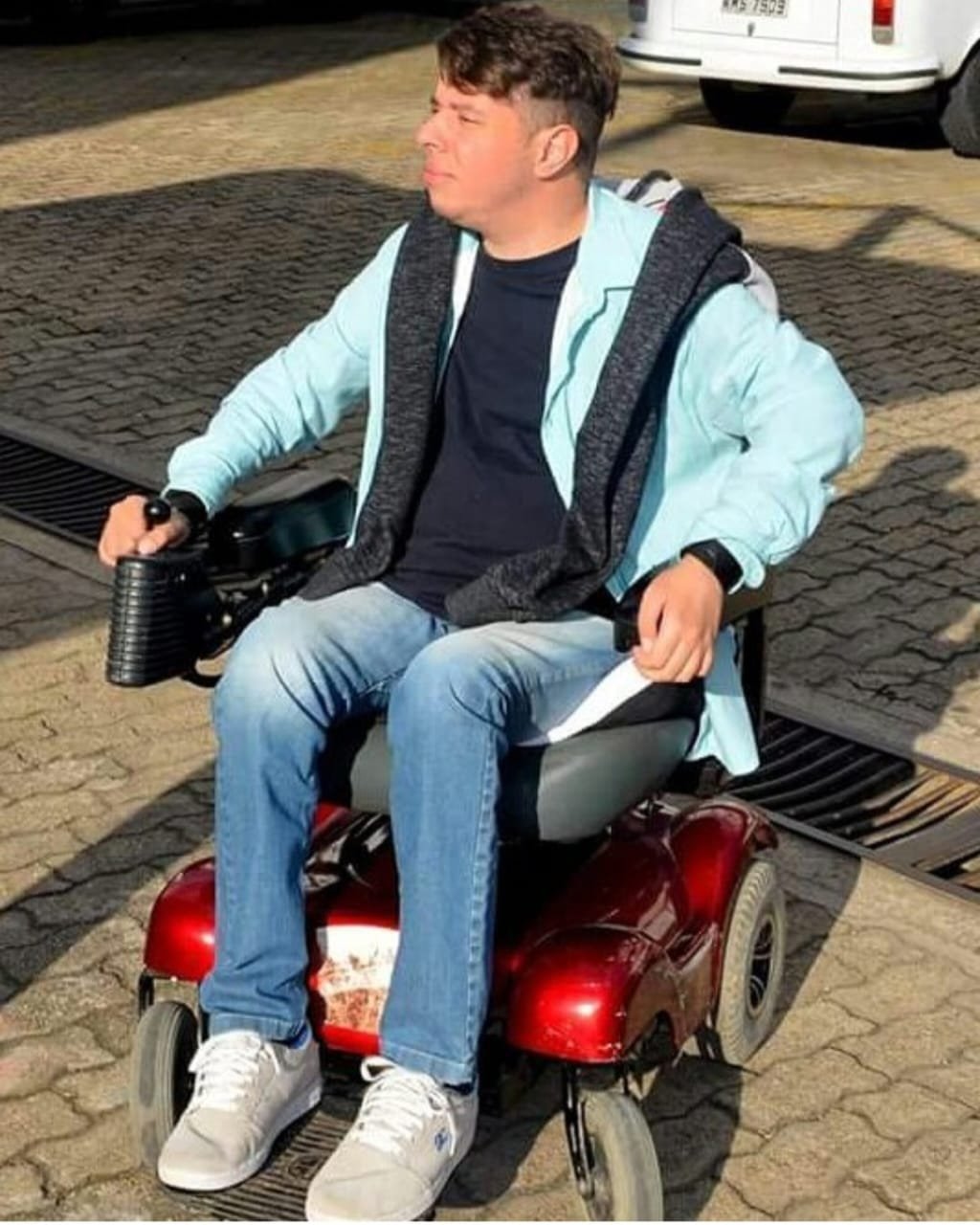 Berguim em sua cadeira de rodas motorizada atual, já bastante desgastada, em um estacionamento.